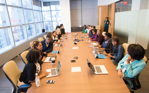 People seated around a long conference table with laptops in a meeting